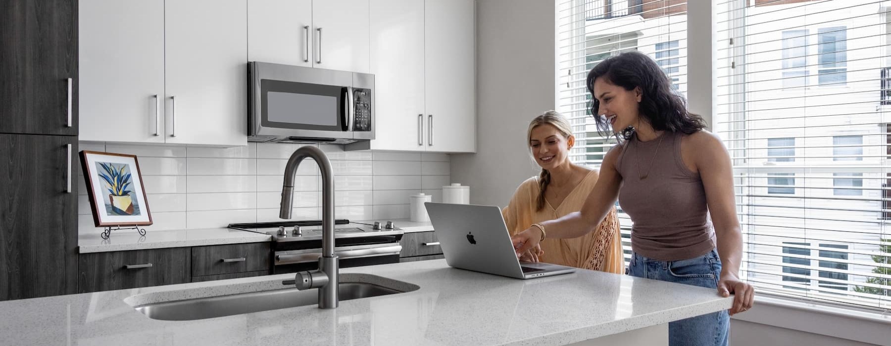 two women looking onto a laptop in a bright kitchen