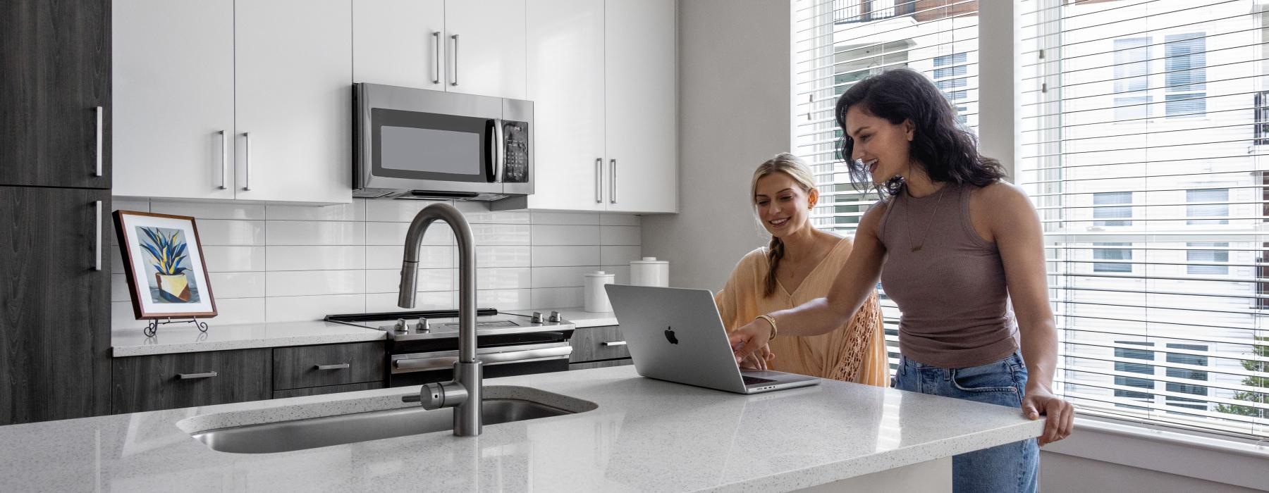 a couple of women looking at a computer on the kitchen counter